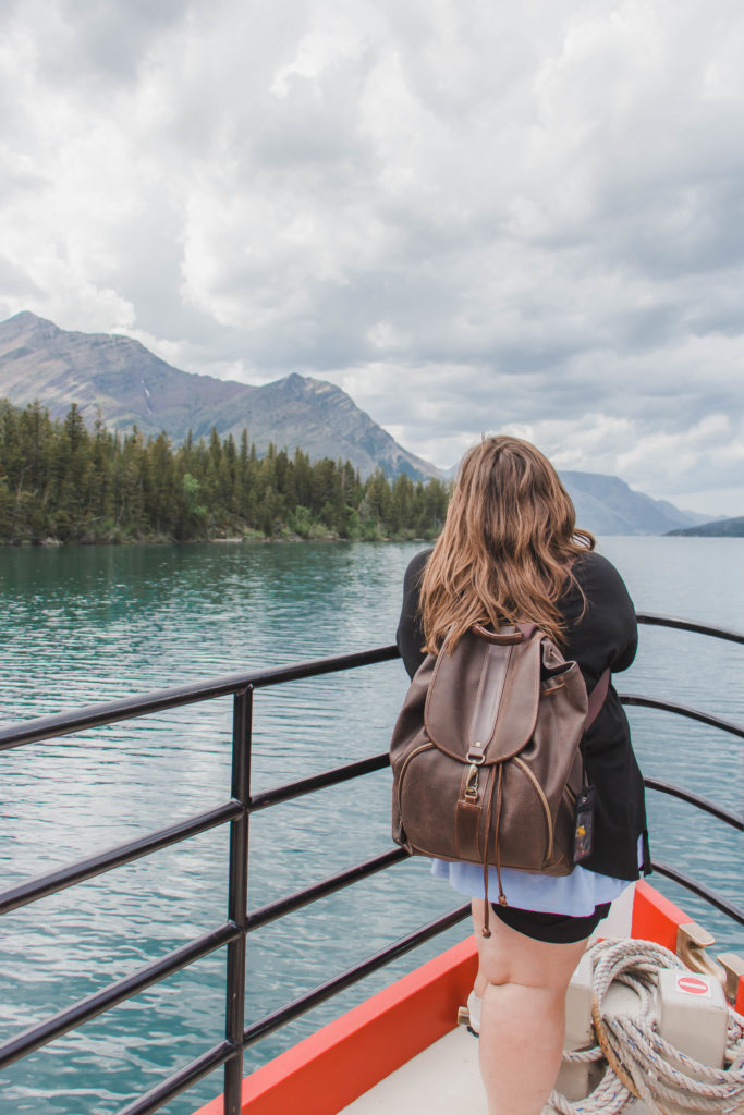 Girl standing on a boat lookin at mountains and Waterton lake