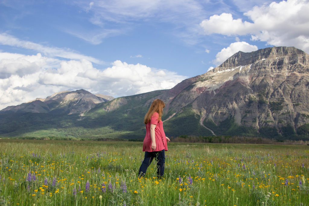 Girl in Wildflower field with mountains and blue sky in waterton alberta canada