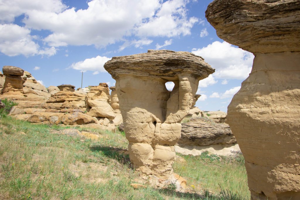 Hoodoo rock formation with hole in it with blue sky and clouds and green grass in writing on stone provincial park