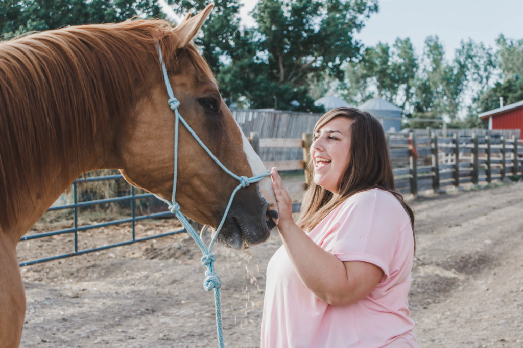 Girl petting brown horse with bokeh farm background