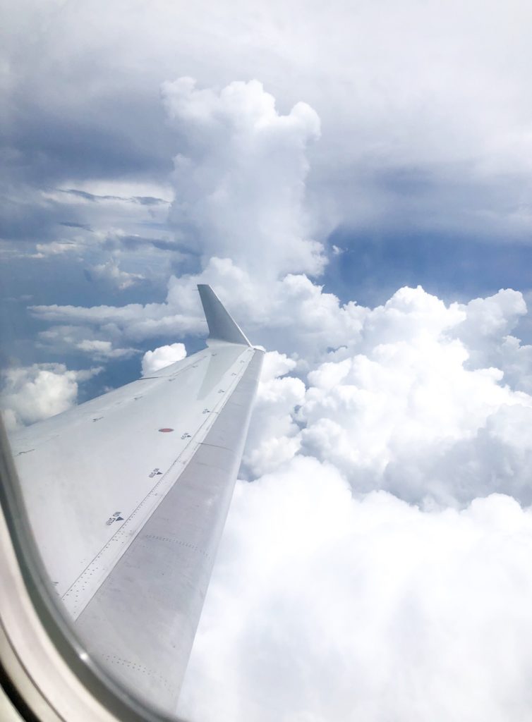 airplane wing, blue sky, and fluffy white clouds outside plane window