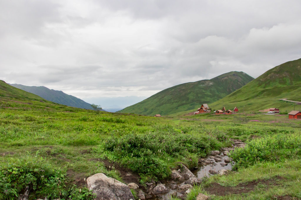 Hatcher Pass lodge red buildings with green mountains and grass and stream