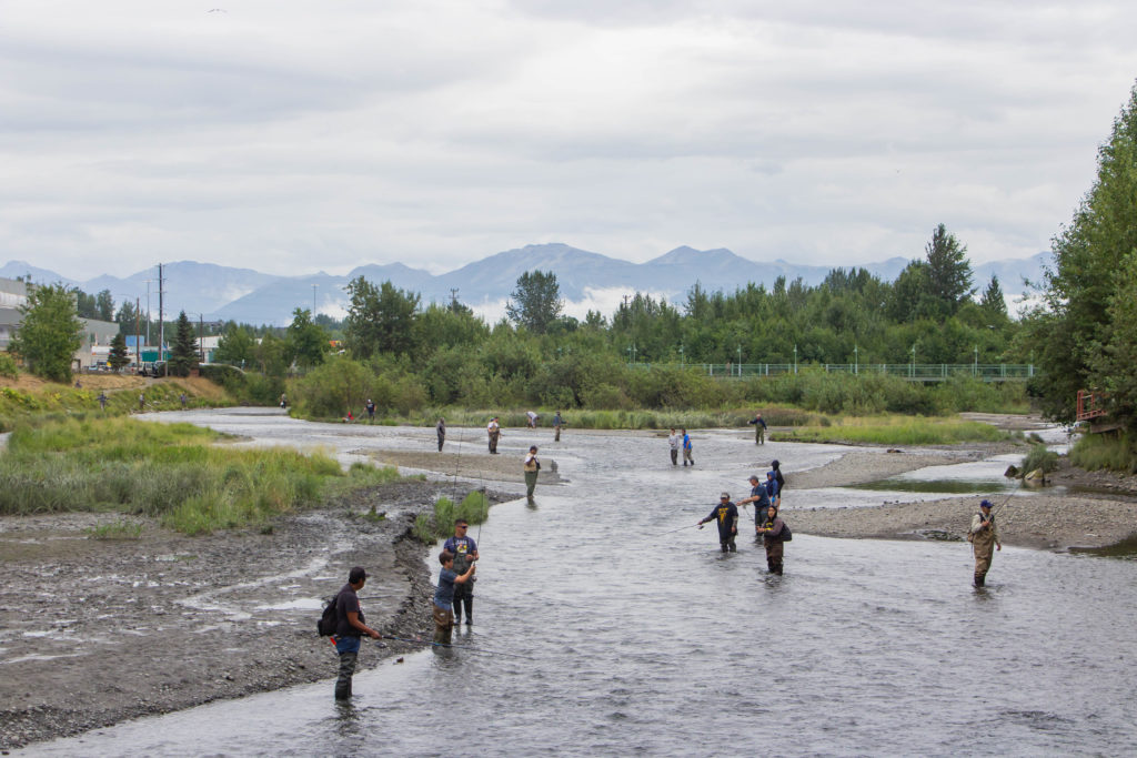 fishermen standing in river in anchorage alaska with mountains fishing for salmon