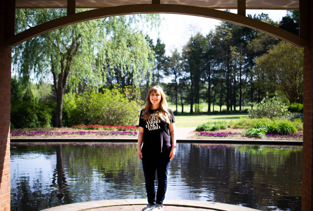 girl in t shirt and jeans in front of pond, flowers, and trees in hunstville botanical garden alabama