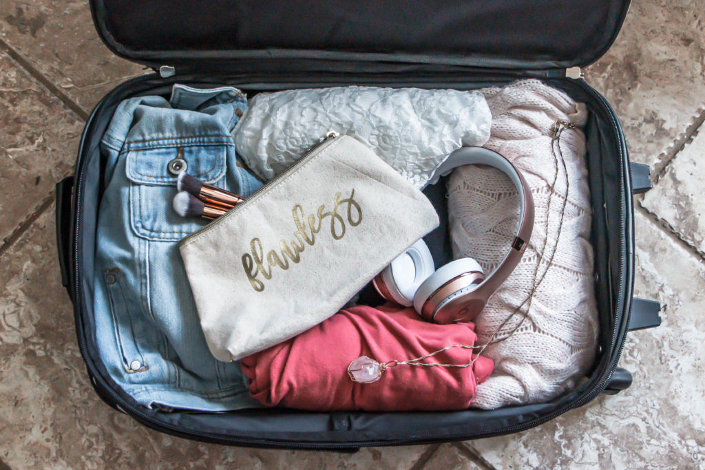 tips for packing a carry on suitcase like a pro beats headphones, denim, pink shirt and necklace, and flawless makeup bag in luggage