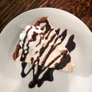 peanut butter pie with chocolate syrup and whip cream on white plate on wooden table at claunch cafe in tuscumbia alabama