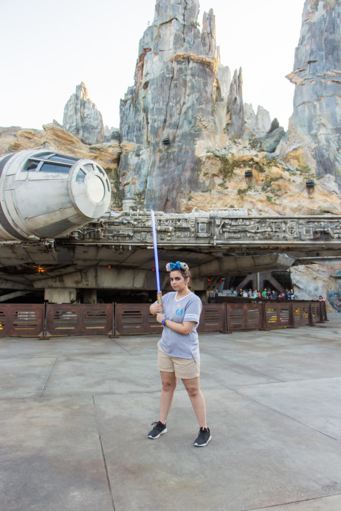 girl with gray t shirt and khaki shorts with blue custom lightsaber in front of millenium falcon at Star Wars galaxy's edge Disney World Hollywood Studios Orlando Florida