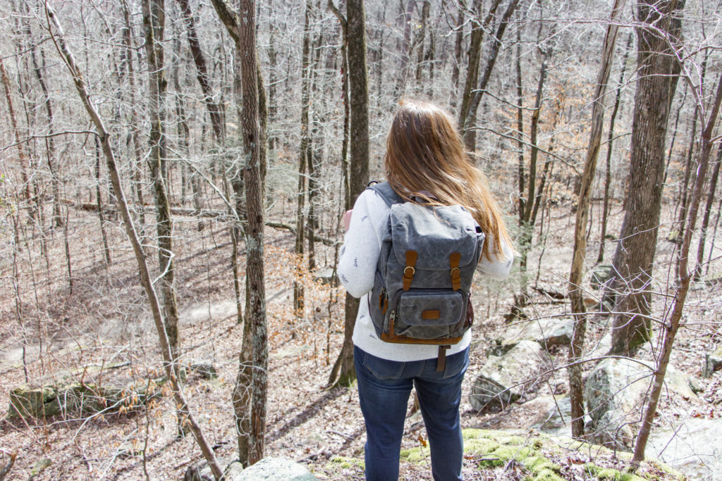 girl with backpack looking at forest woods exploring the trees while hiking